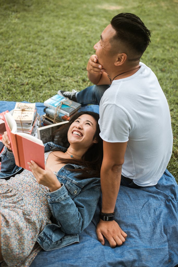 Asian couple having a joyful picnic reading books together on a sunny day in the park.